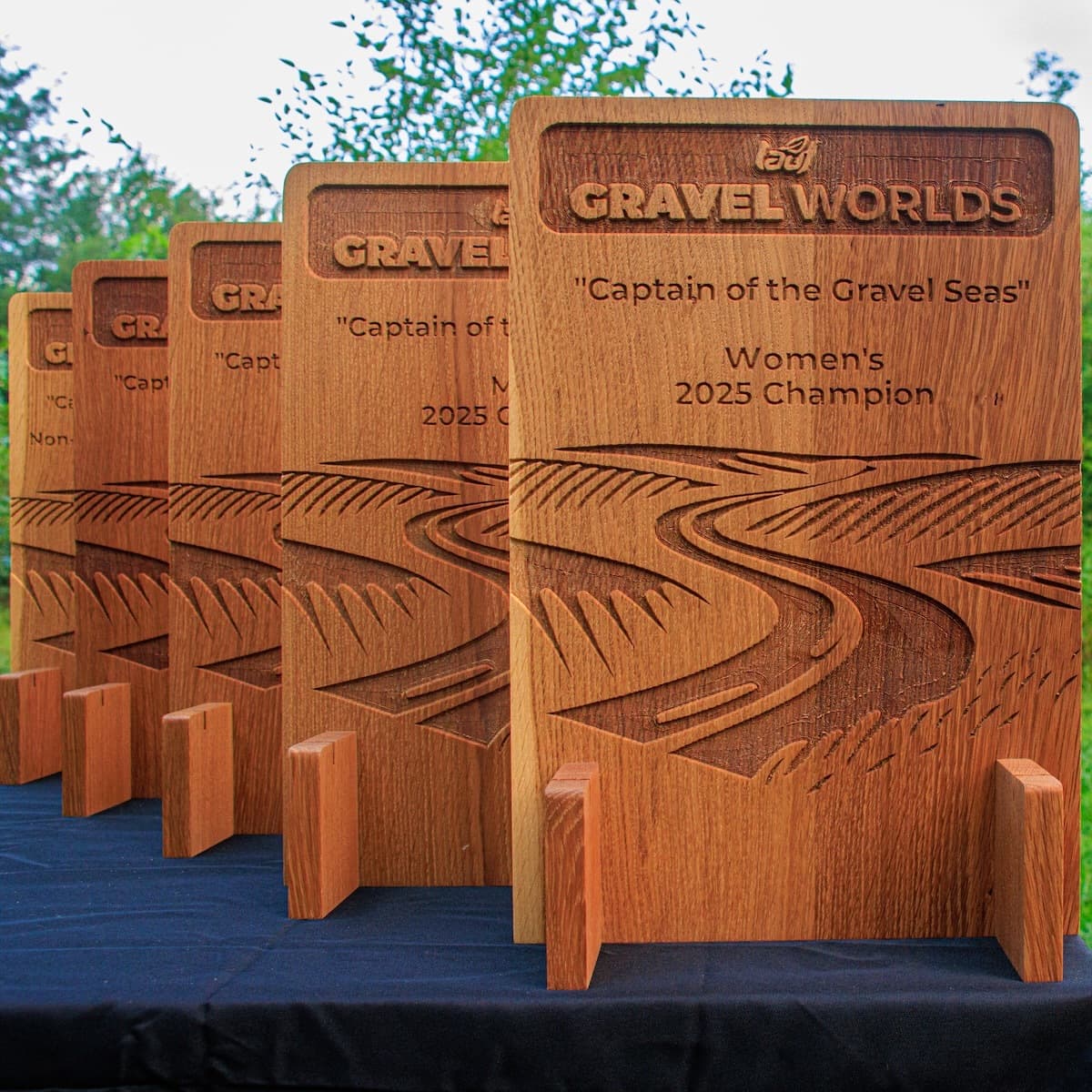 Close-up detail of Gravel Worlds trophy showing engraved text, logo, and flowing sword graphic design in white oak