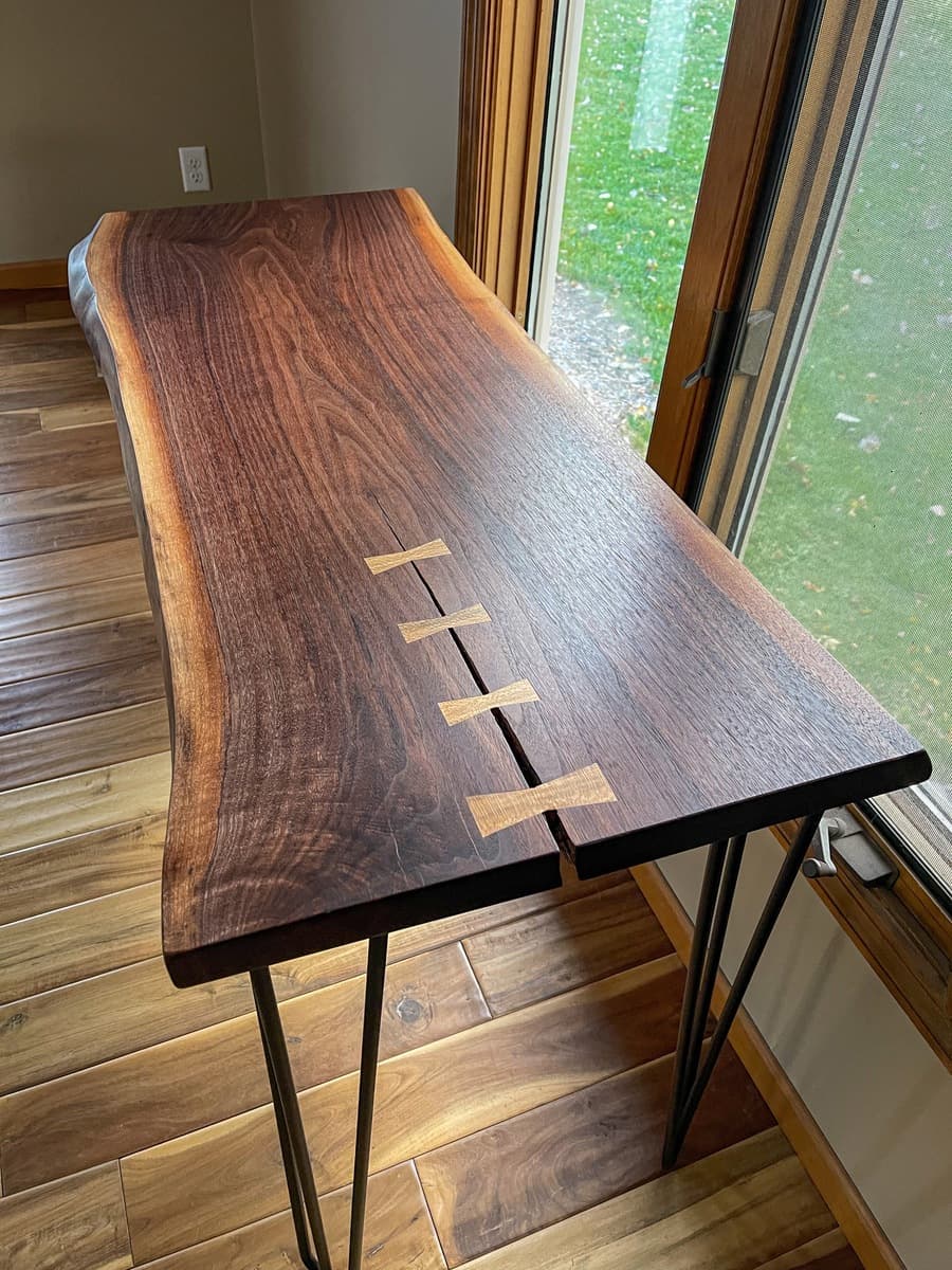 Aerial view of walnut console table displaying full live-edge slab top with four sycamore bowties, black hairpin legs, and natural bark edge along one side.